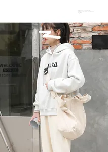 Detail view of a large beige canvas bag worn crossbody by a model in a casual setting.