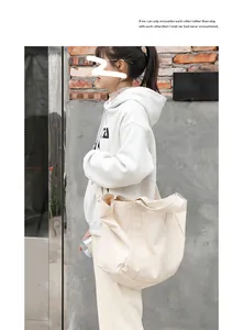Side view of a large beige canvas shoulder bag worn by a model in casual attire