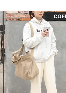 Large khaki canvas shoulder bag worn by a model in a casual lifestyle setting.