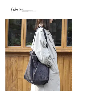 Model carrying a large charcoal corduroy shoulder bag over a beige trench coat