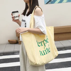 Casual pale yellow nylon tote bag with green letter print shown on model in street