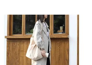 Lifestyle detail of a large beige corduroy shoulder bag carried by a model in a trench coat