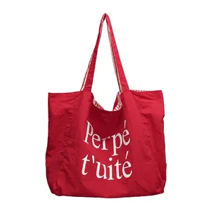 Red nylon tote bag with white Perpétuité print and striped handles