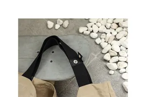 Dettaglio della tracolla in tela nera con bottone a pressione su una borsa tipo kaki