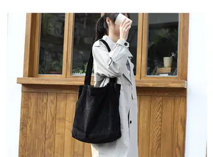Large minimalist black corduroy tote bag worn by a model in a natural outdoor lifestyle scene