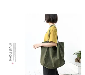 Side view of model carrying a large olive green washed canvas tote bag in a minimalist setting