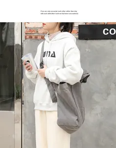 Model carrying a large grey canvas crossbody bag in a stylish outdoor street scene