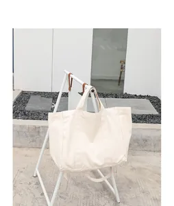 Large cream-colored canvas tote bag displayed on a minimalist white stand in daylight