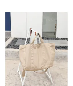 Detail of a large beige canvas tote bag hanging on a white outdoor stand for display.