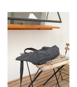 A detailed view of a minimalist washed black canvas shoulder bag placed on a rustic wooden table