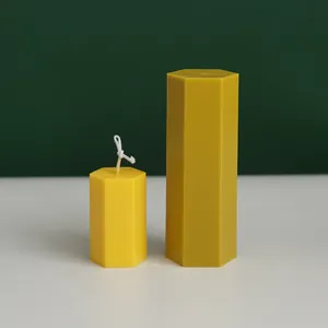 Detail of two yellow hexagonal candles in different heights against green backdrop.