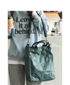 Vintage green washed kraft paper tote bag shown in a stylish lifestyle street setting.