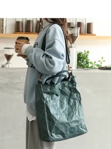 Detailed view of a dark green washed kraft paper tote bag worn by a model in a cafe
