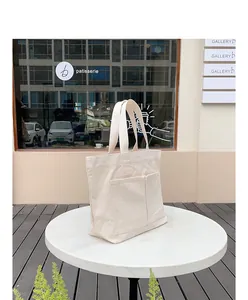 Minimalistische cremefarbene Canvas-Einkaufstasche mit zwei Außentaschen auf einem Tisch