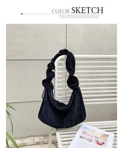 A detailed view of a black corduroy shoulder bag with a unique ruffled handle design