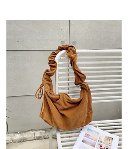 Detail view of a brown corduroy bag with a stylish pleated strap on a white bench