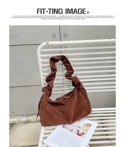 Detail of brown corduroy shoulder bag with stylish ruched handle on white metal chair