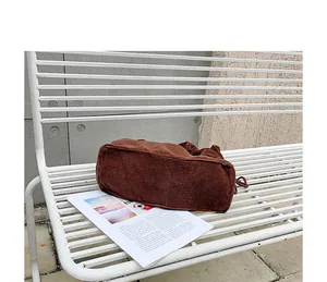 Close-up view of a brown corduroy shoulder bag with drawstring detail on white metal bench