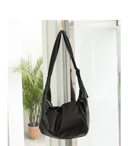 Bolso de hombro de cuero PU negro plisado colgado en un ambiente interior moderno.