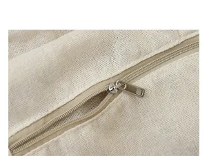 Detailed close-up of the smooth metal zipper on a minimalist cream nylon shoulder bag