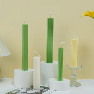 Velas de pilar acanaladas minimalistas en verde, blanco y amarillo sobre pedestales blancos.