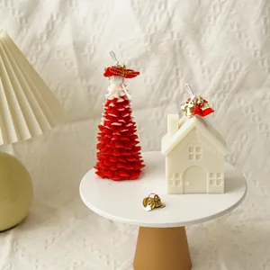 Detailed view of red Christmas tree and white house shaped candles on a white display stand