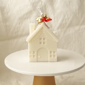Detail of house-shaped cream scented candle with festive red bow and gold bells
