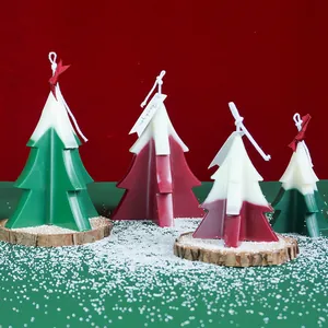 Handmade Christmas tree candles with snowy tops on a festive red and green background