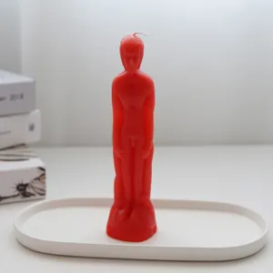 Close-up of a red male figure candle placed on a minimalist white oval tray