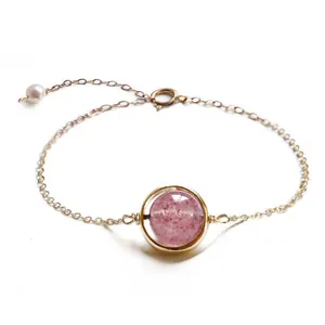 Close-up of elegant strawberry quartz bracelet with gold chain and pearl charm detail.