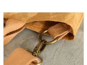 Detailed view of the antique brass buckle and canvas strap on a kraft paper bag