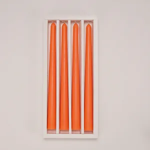 Top view of four long orange tapered candles neatly arranged in a white gift box