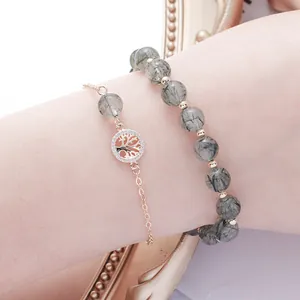 Green rutilated quartz beaded bracelet set with golden Tree of Life charm worn on wrist