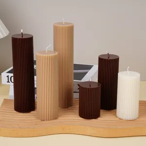 Close-up view of various earth-toned ribbed pillar candles on a decorative wavy wooden tray.