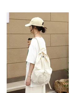 Rückansicht eines Modells mit einem cremefarbenen Nylon-Rucksack im Freien.