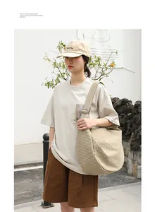 Modelo luciendo un gran bolso tipo dumpling de lona beige a cuadros en un entorno urbano
