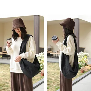 Model wearing a black denim dumpling bag and brown bucket hat in a sunny outdoor garden