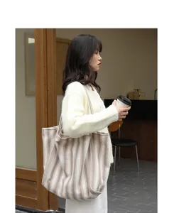 Dettaglio lifestyle di una grande borsa tote in tela a righe indossata da una modella.