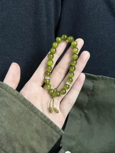 Detail of an elegant olive green cat eye beaded bracelet held in hand with Zen style