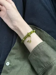 Detail of olive green cat-eye beaded bracelet worn on wrist with green linen shirt