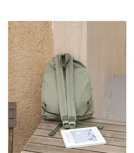 Rückansicht eines olivgrünen Rucksacks aus Nylon mit Kordelzug auf Holztisch.