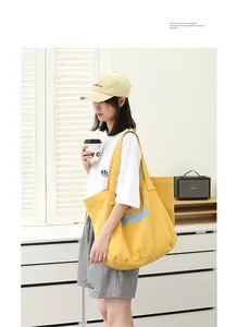 Asian model carries a vibrant yellow canvas tote bag with blue lettering in a room.