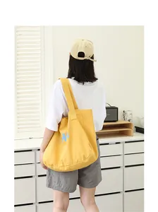 Model wearing a yellow canvas tote bag with blue letter print in a bright room
