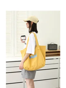 Lifestyle detail showing a yellow canvas tote bag with 'Hai' print carried by a model.
