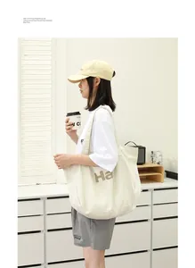 Large canvas tote bag with letter print carried by a model in a minimalist room