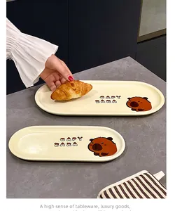 Détail de jolies assiettes à dessert ovales en céramique avec motif capybara et croissant.