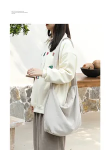 Detail view of a cream minimalist corduroy hobo shoulder bag worn by a model in a park