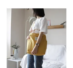 Detailed lifestyle view of a minimalist yellow canvas tote bag held by a model in a room.