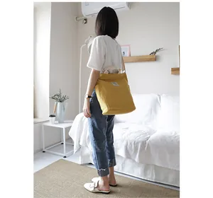Close-up of the yellow canvas shoulder bag in a lifestyle setting worn by a fashion model