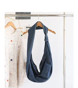 Stylish denim hobo bag with unique knotted strap detail hanging on a garment rack
